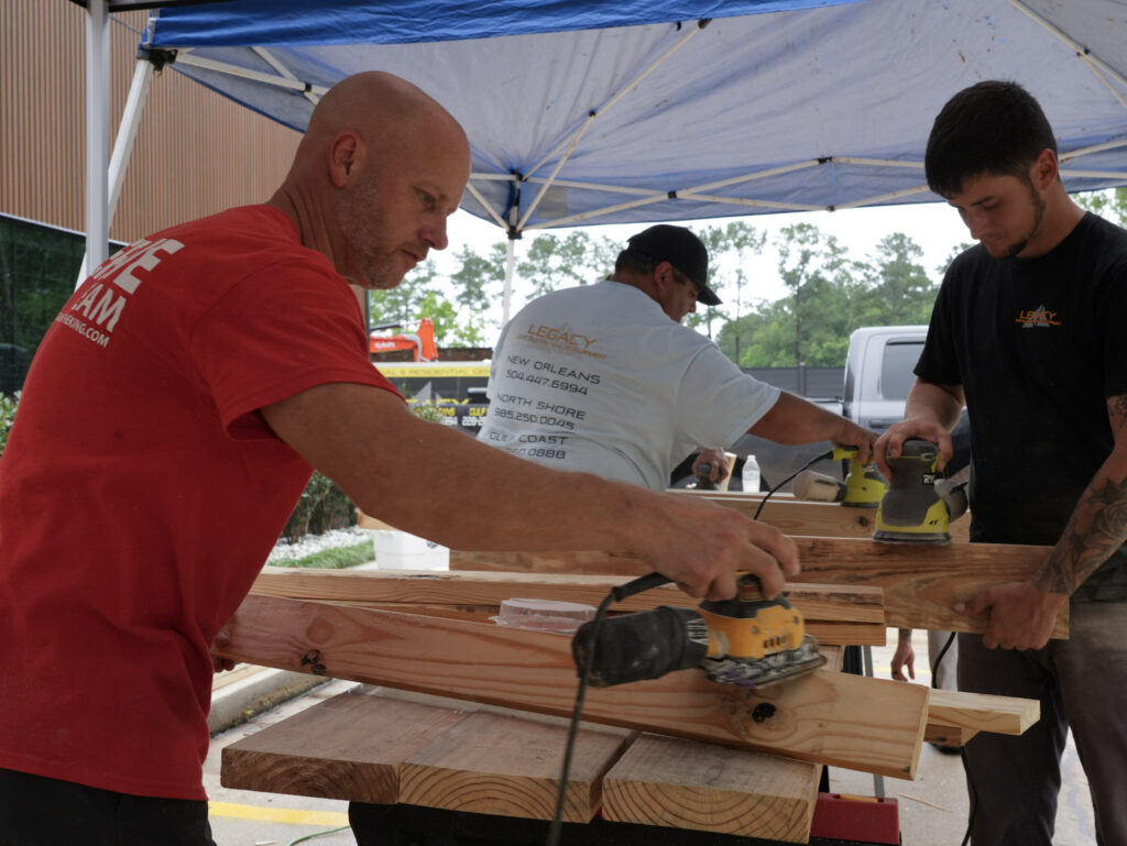 Impact Day 2026: Building More Than Beds 12 Legacy Construction crew and Church of the King volunteers sanding wooden bed frames during Legacy Day 2026