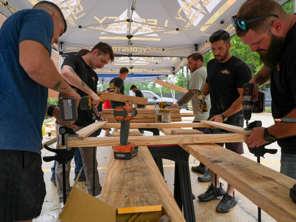 Impact Day 2026: Building More Than Beds 1 Legacy Construction and Development crew assembled under branded canopy tents for Legacy Day 2026, a community giveback event in Louisiana