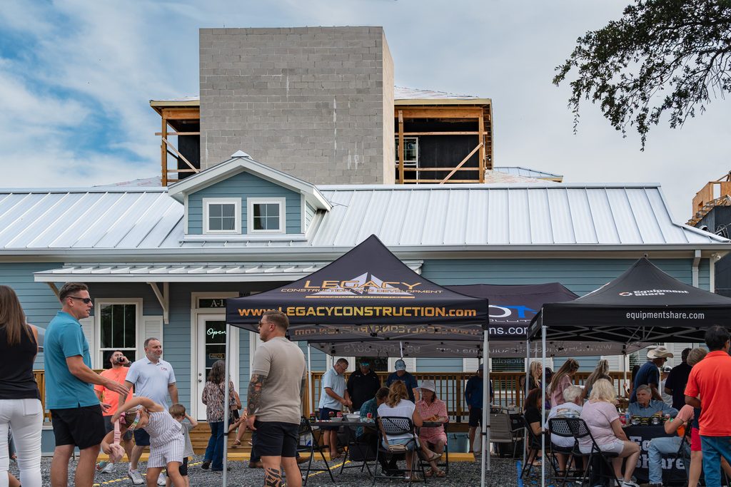 Guests gather beneath a Legacy Construction & Development tent at Eagan’s topping-out celebration in Pass Christian, MS.