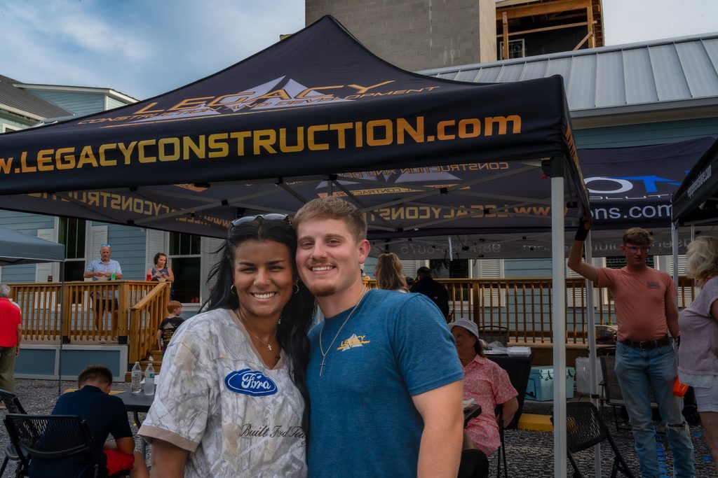 Two smiling guests pose beneath the Legacy Construction & Development tent at Eagan’s topping-out celebration.