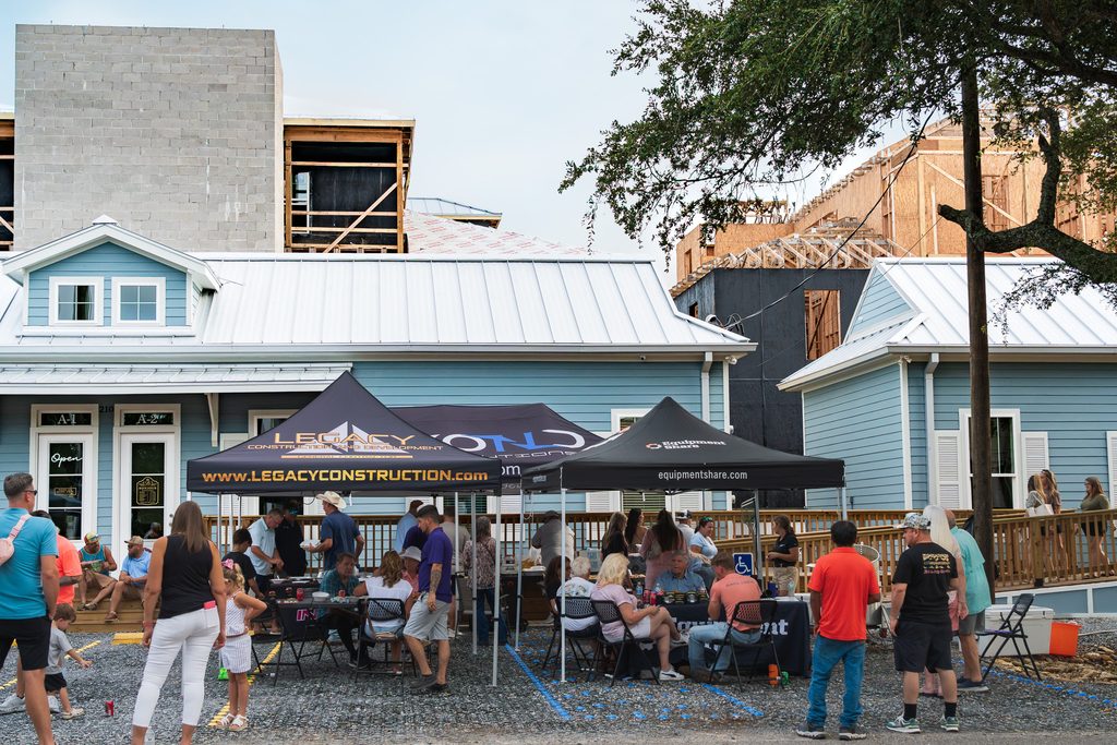 Guests share food and conversation outside Eagan’s blue storefronts, with the development under construction behind them.