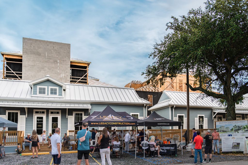 Wide view of Eagan’s topping-out party with event tents, storefronts, a large oak tree and the development’s exposed framing.