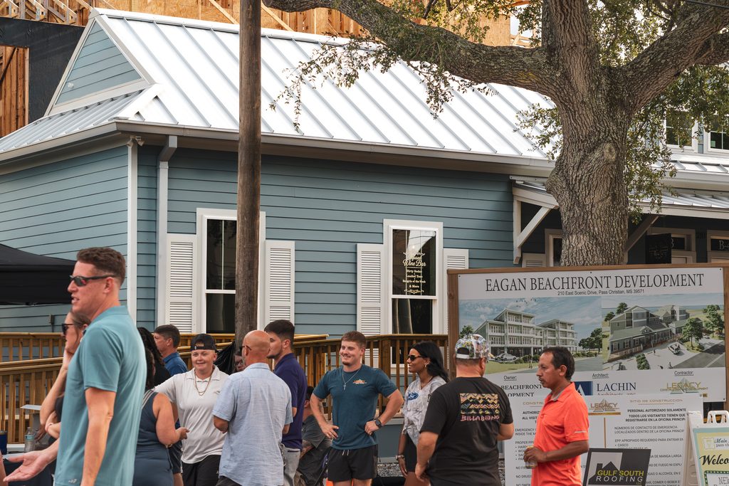 Guests chat beside the Eagan Beachfront Development sign displaying architectural renderings in Pass Christian, MS.