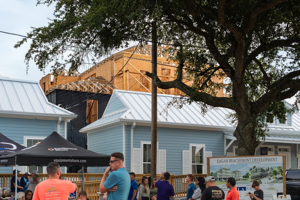 Exposed wood framing and roof trusses rise behind Eagan’s blue storefronts as guests gather for the topping-out celebration.